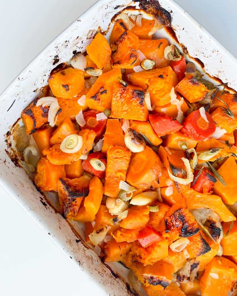 roasted butternut squash carrots fennel garlic onions apple and herbs in a white baking dish