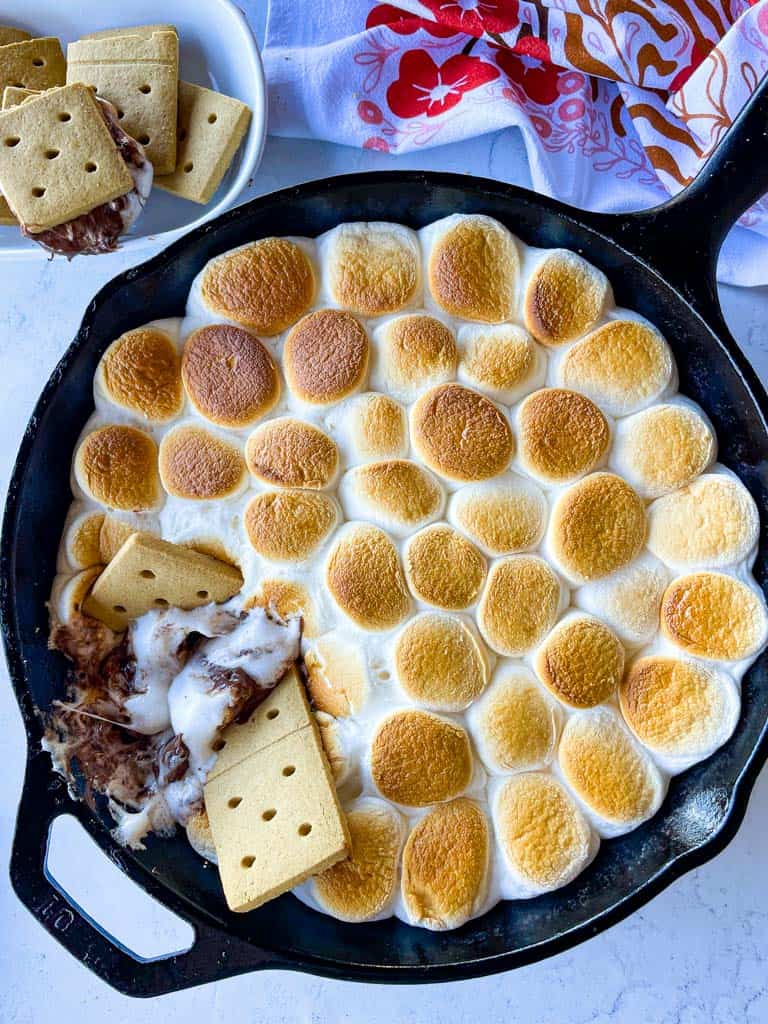 a skillet full of s'mores dip with a bowl of graham crackers