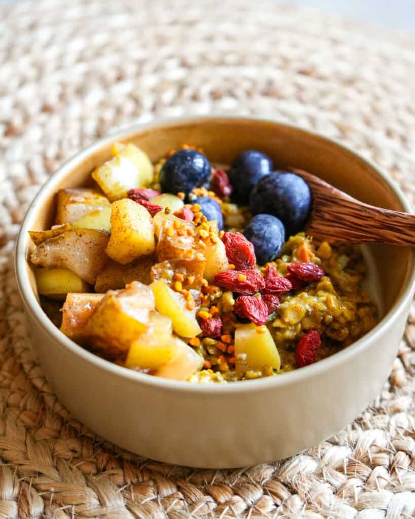 golden turmeric oatmeal in a small bowl with toppings and a spoon