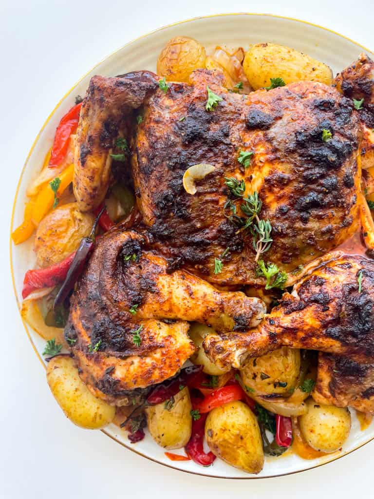 close up view of spatchcock chicken on a platter with potatoes and peppers