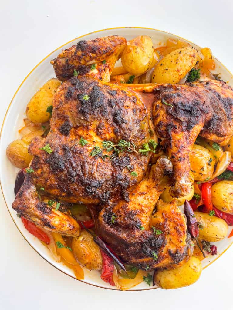 close up view of a whole baked cajun chicken on a platter surrounded by veggies and potatoes