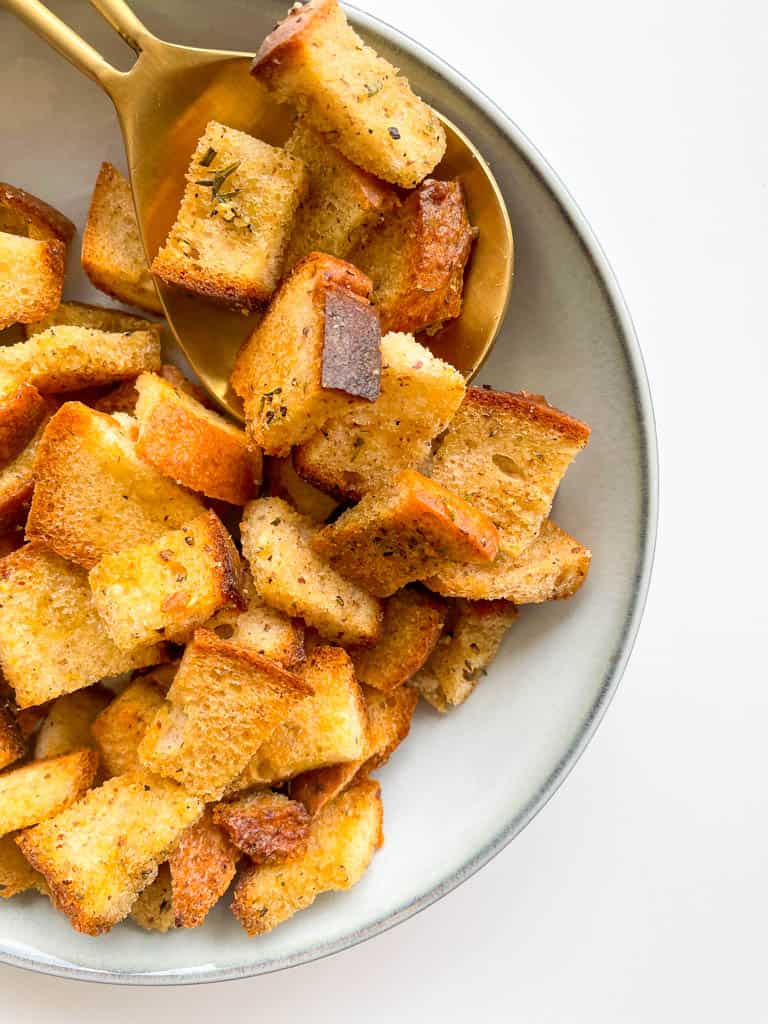 Homemade Gluten Free Croutons in a white bowl with a large gold spoon in the bowl with croutons on top