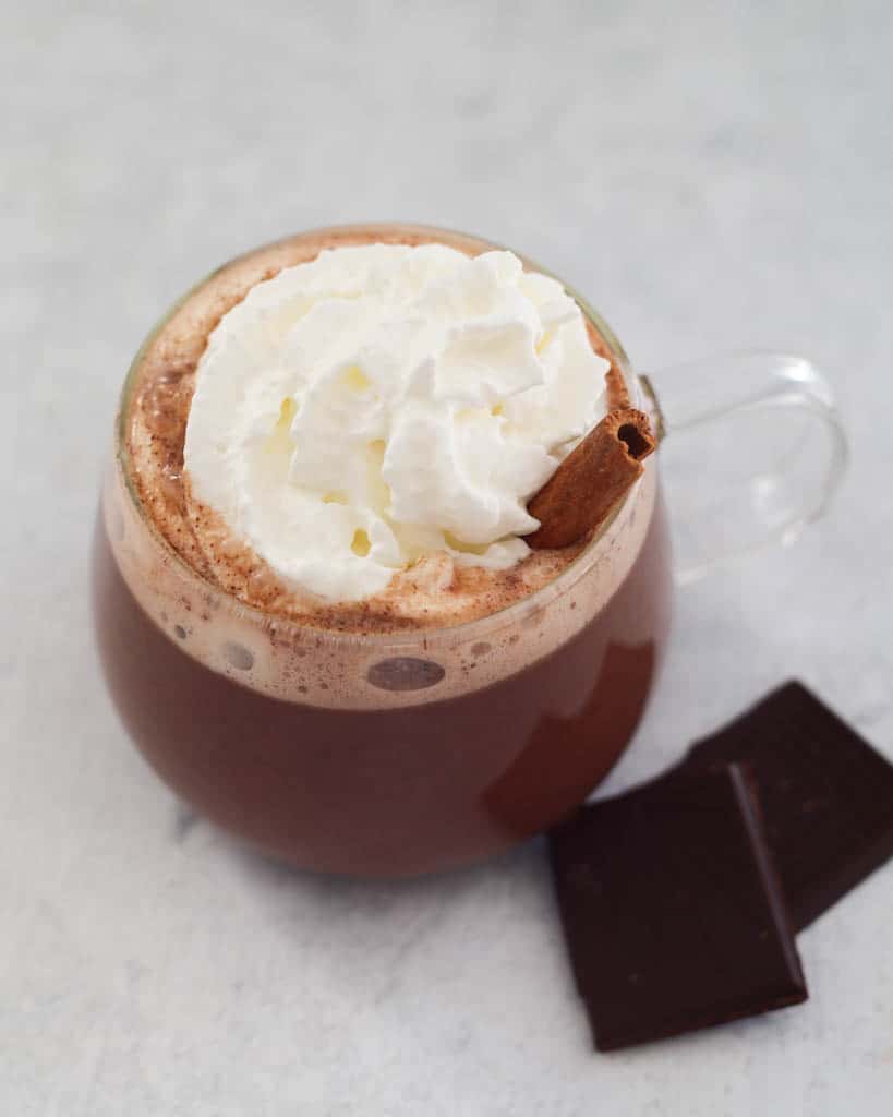 clear mug of vegan oat milk hot chocolate with coconut whipped cream