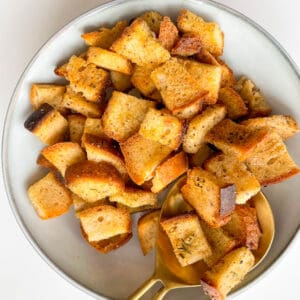 Homemade Gluten Free Croutons in a white bowl with a large gold spoon in the bowl with croutons on top