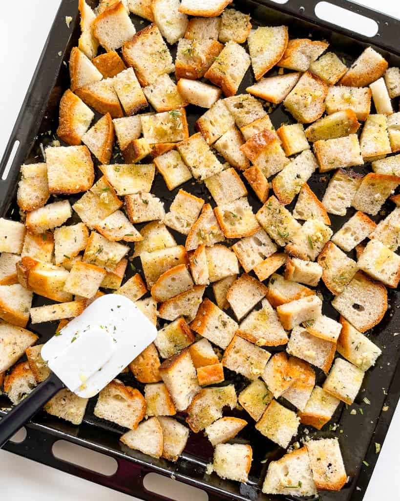 sliced bread cubes on a sheet tray with rubber spatula on the tray
