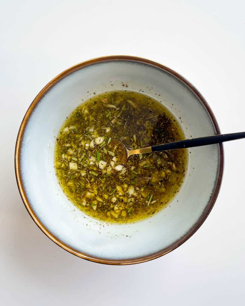 olive oil garlic herb mixture in a small white bowl with small spoon