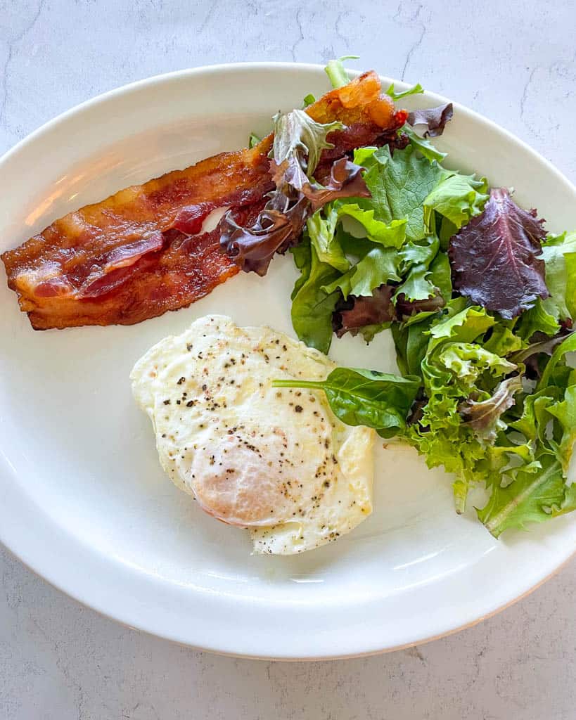 plate of bacon, one egg, and salad
