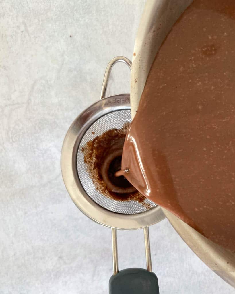 straining hot chocolate into a mug through a fine mesh strainer