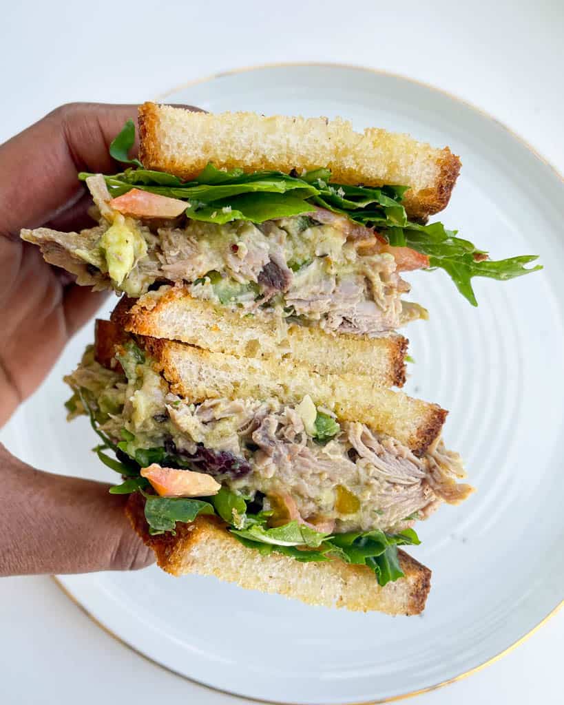 a hand holding a sliced turkey salad sandwich