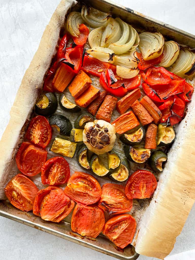 tomatoes zucchini carrots red peppers and onions on a baking dish fully roasted