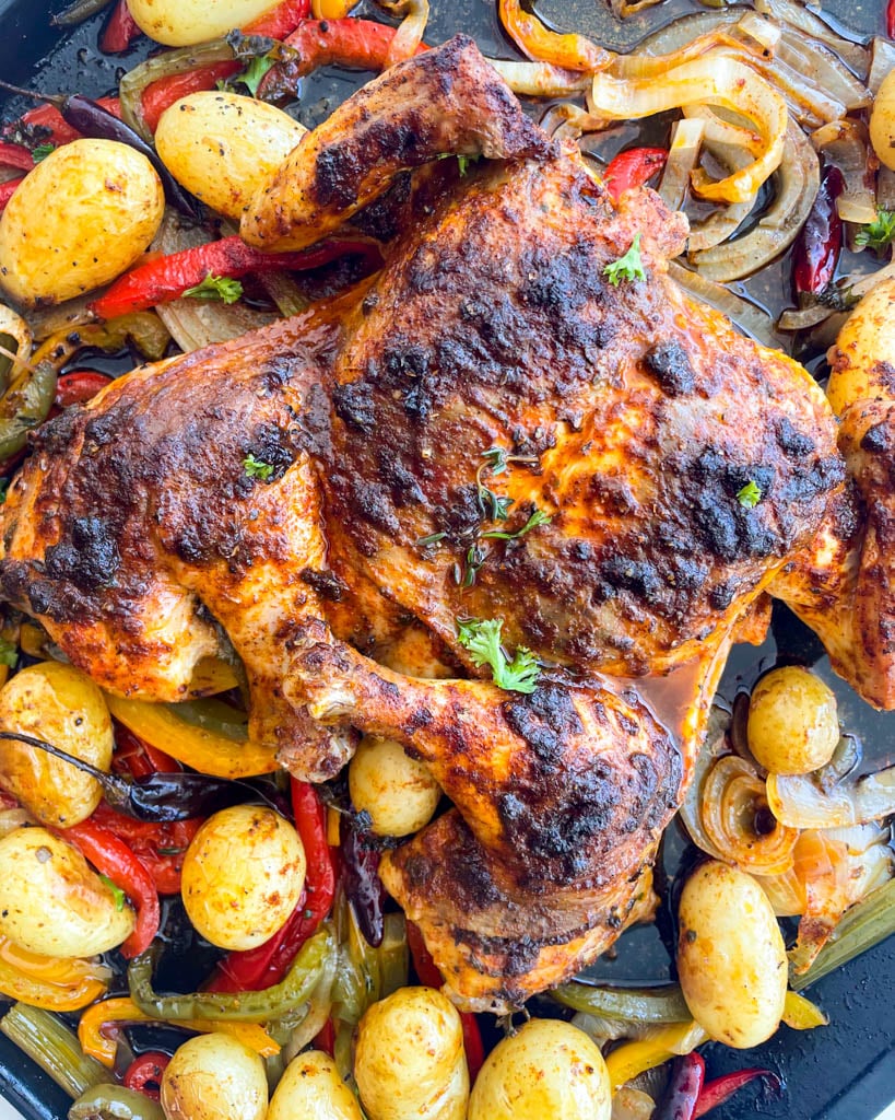 close up view of a whole baked  chicken on a platter surrounded by veggies and potatoes