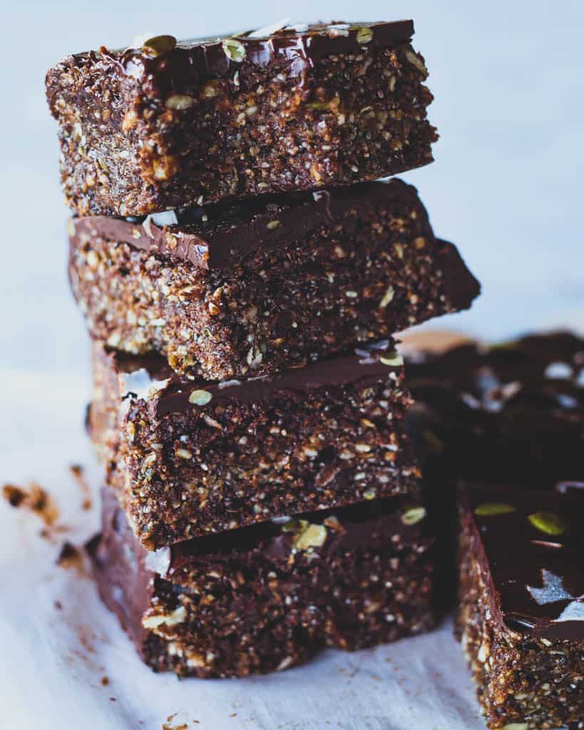 Close up of sliced piece of energy bar with chocolate coating, coconut shavings and pumpkin seeds on top. 