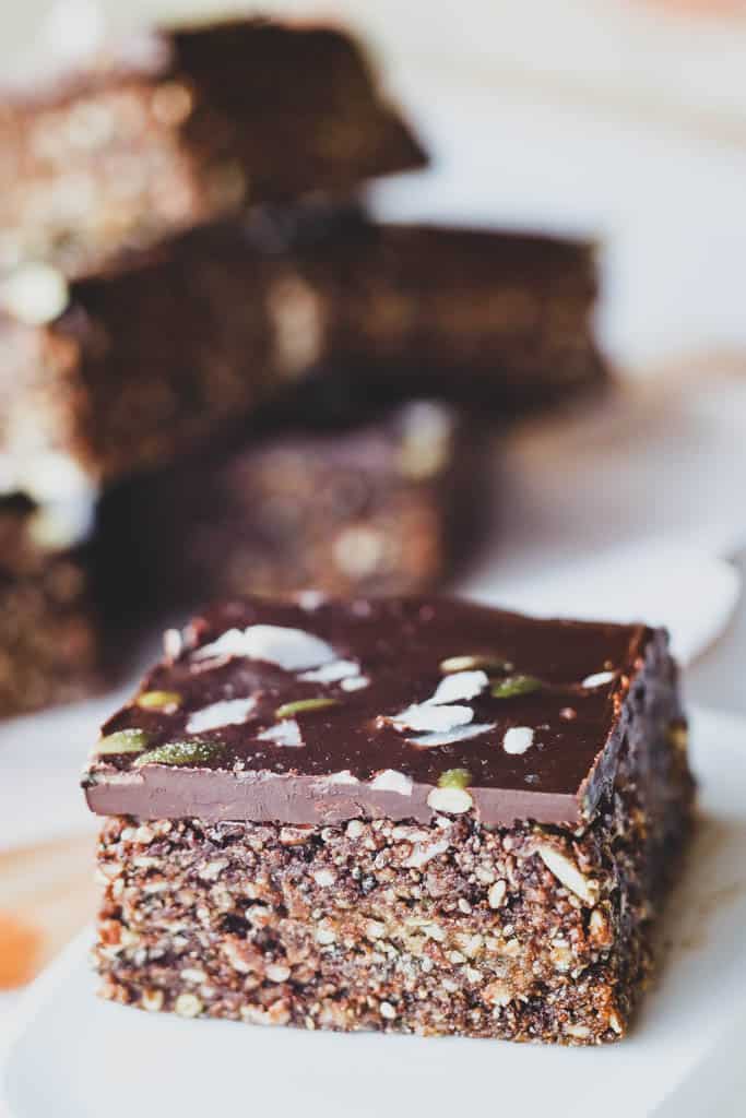 Close up of sliced piece of energy bar with chocolate coating, coconut shavings and pumpkin seeds on top. 