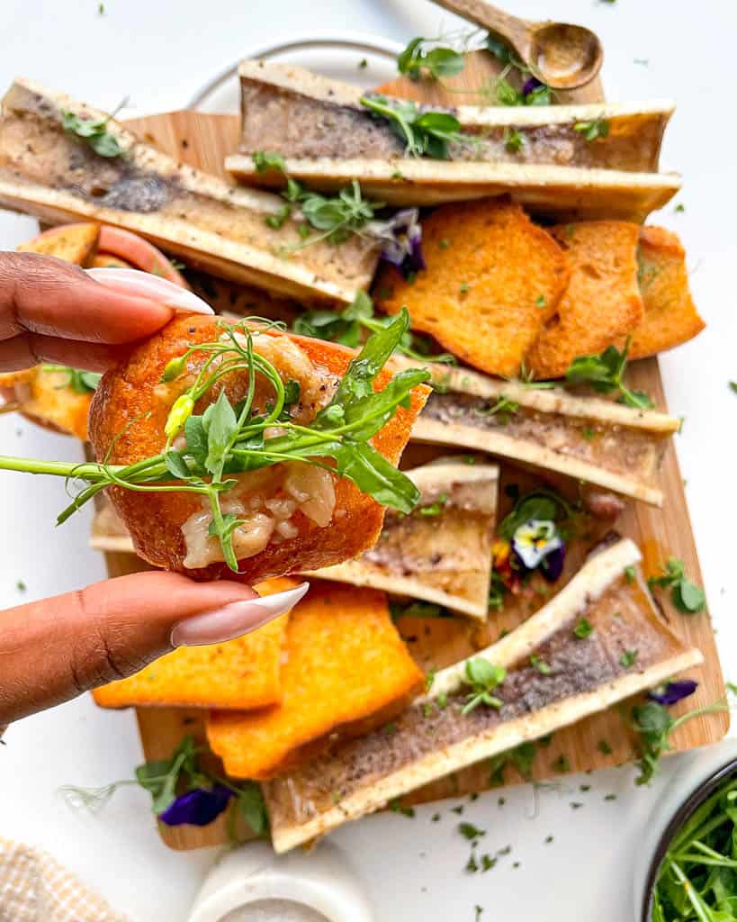 hand holding a toasted piece of bread with bone marrow spread and arugula on top