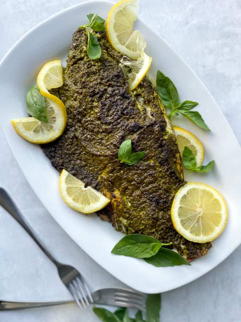 plated pesto-crusted broiled sea bass with sliced lemons for garnish