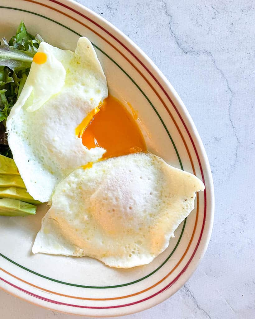 runny yolk alongside a salad and sliced avocado