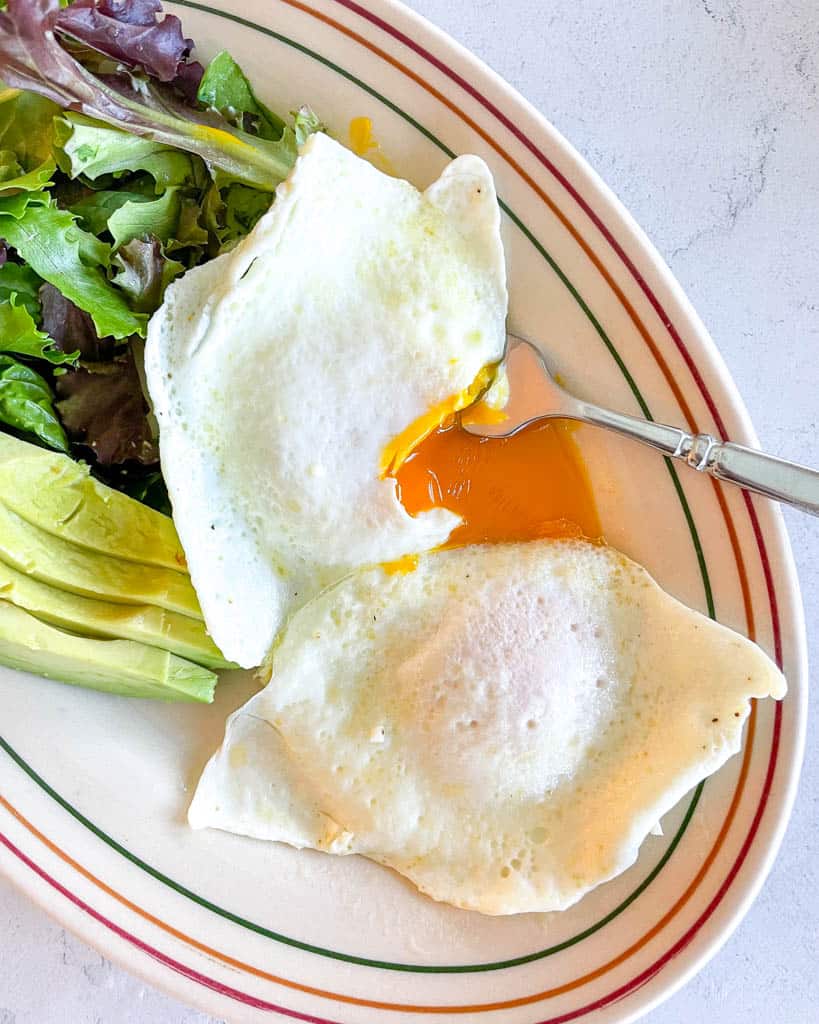 plated over easy eggs alongside a salad and sliced avocado