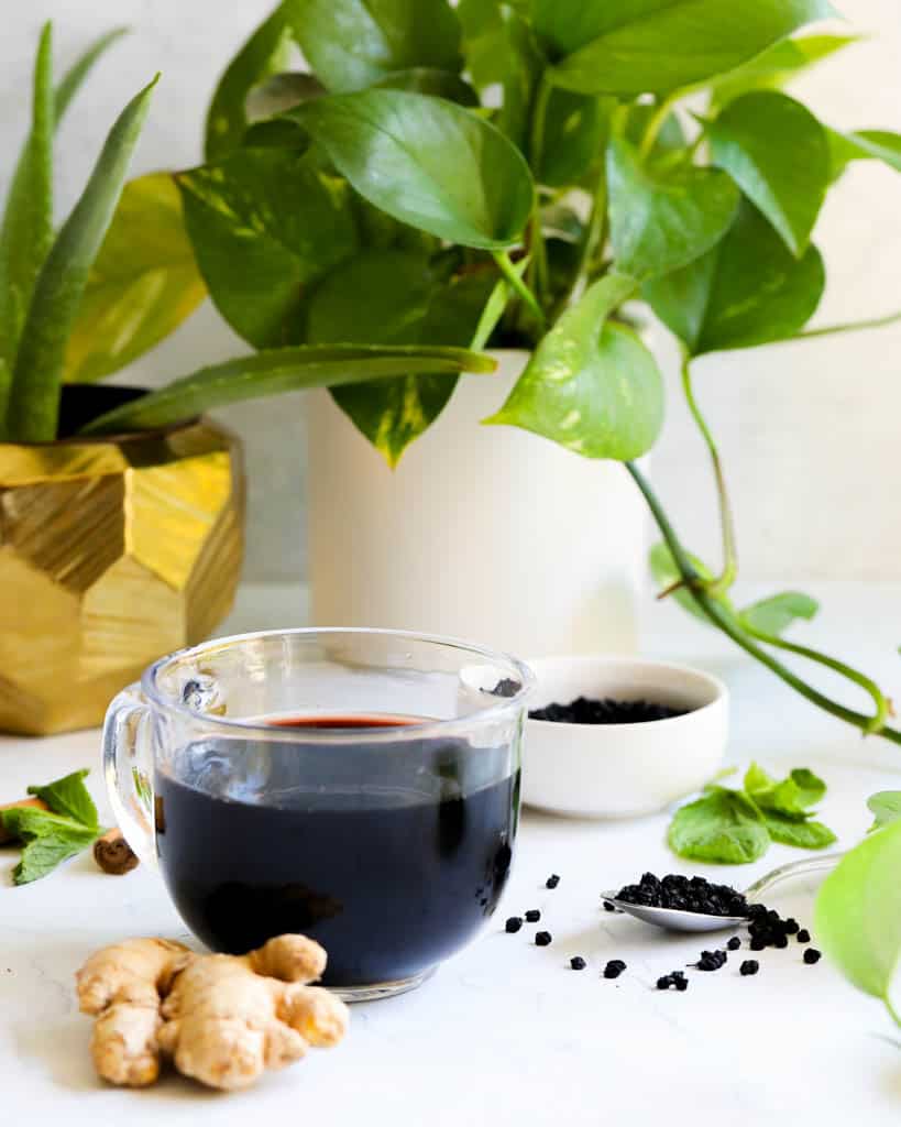 a clear mug full of elderberry tea with plants in the background