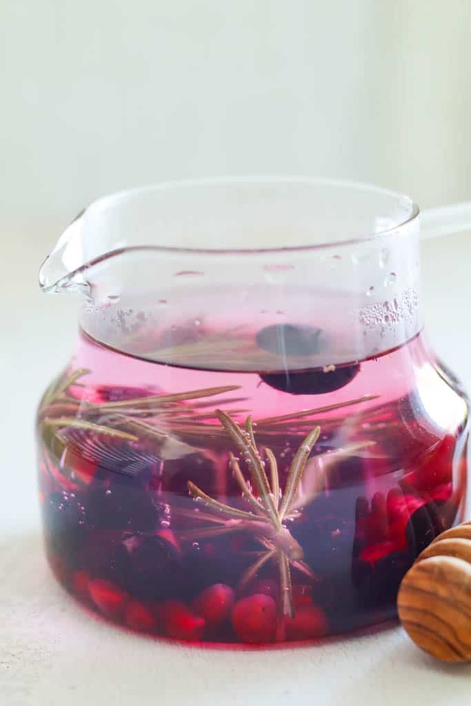 A glass filled with rosemary tea infused with blueberries and pomegranate