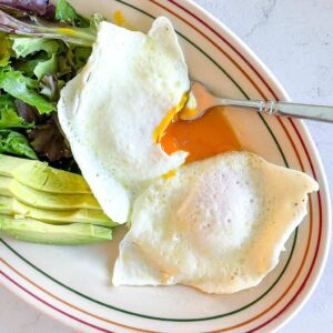 plated over easy eggs cut to reveal runny yolk alongside a salad and sliced avocado
