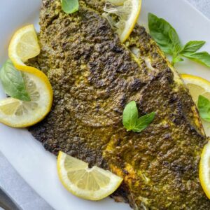 close up view of plated pesto-crusted broiled sea bass garnished with lemon