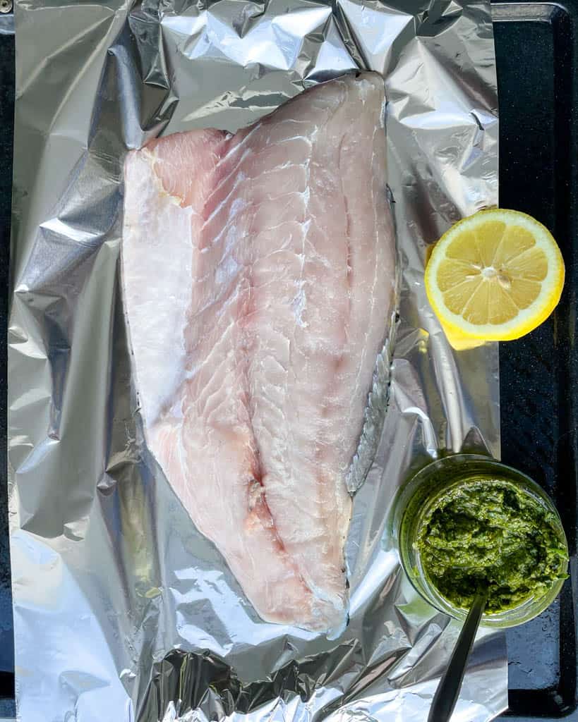 raw sea bass next to a container full of pesto and half a lemon