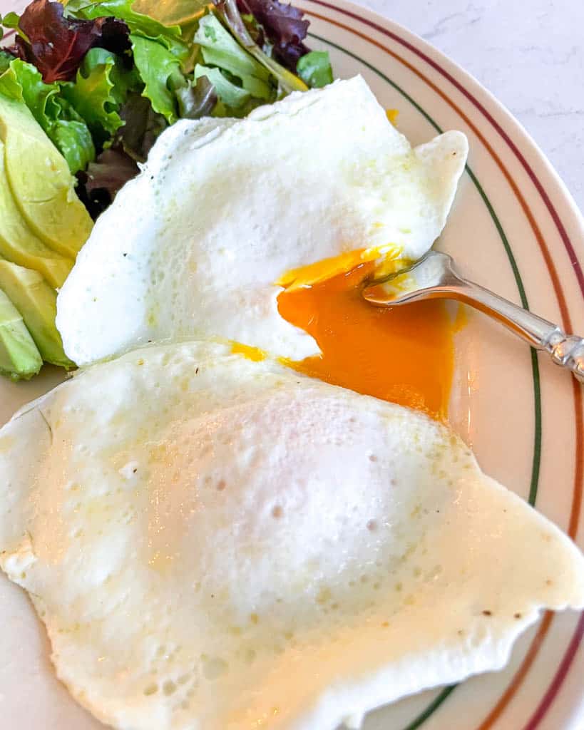 plated over easy eggs alongside a salad and sliced avocado