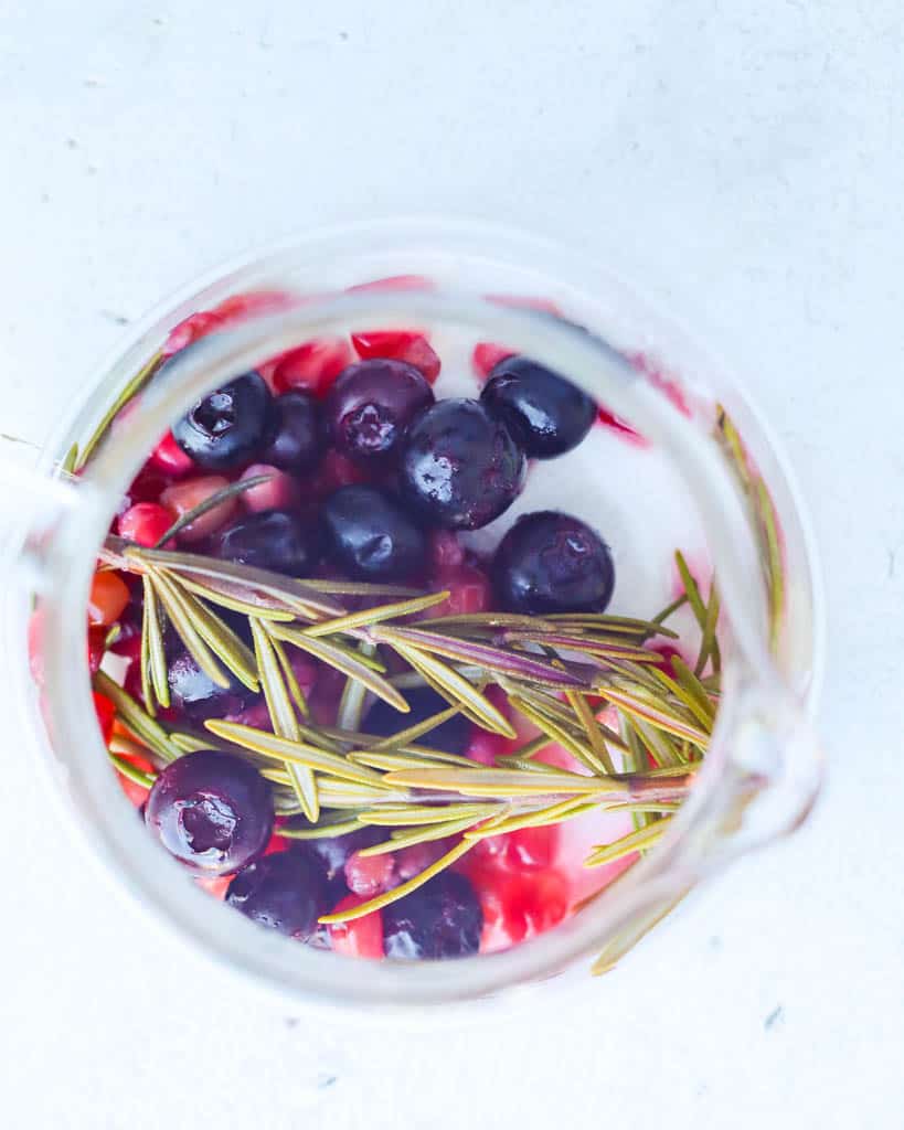 overhead view of rosemary sprigs blueberries and pomegranate in a glass