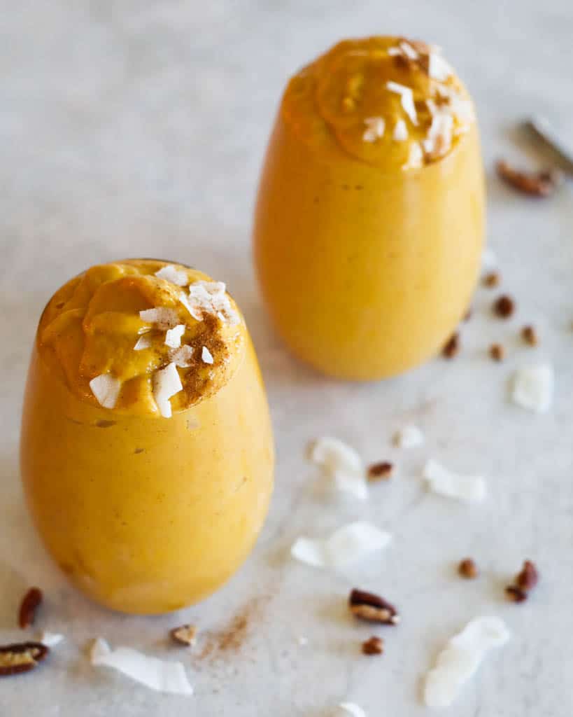 two sweet potato smoothies in glasses and topped with coconut shavings and pecans