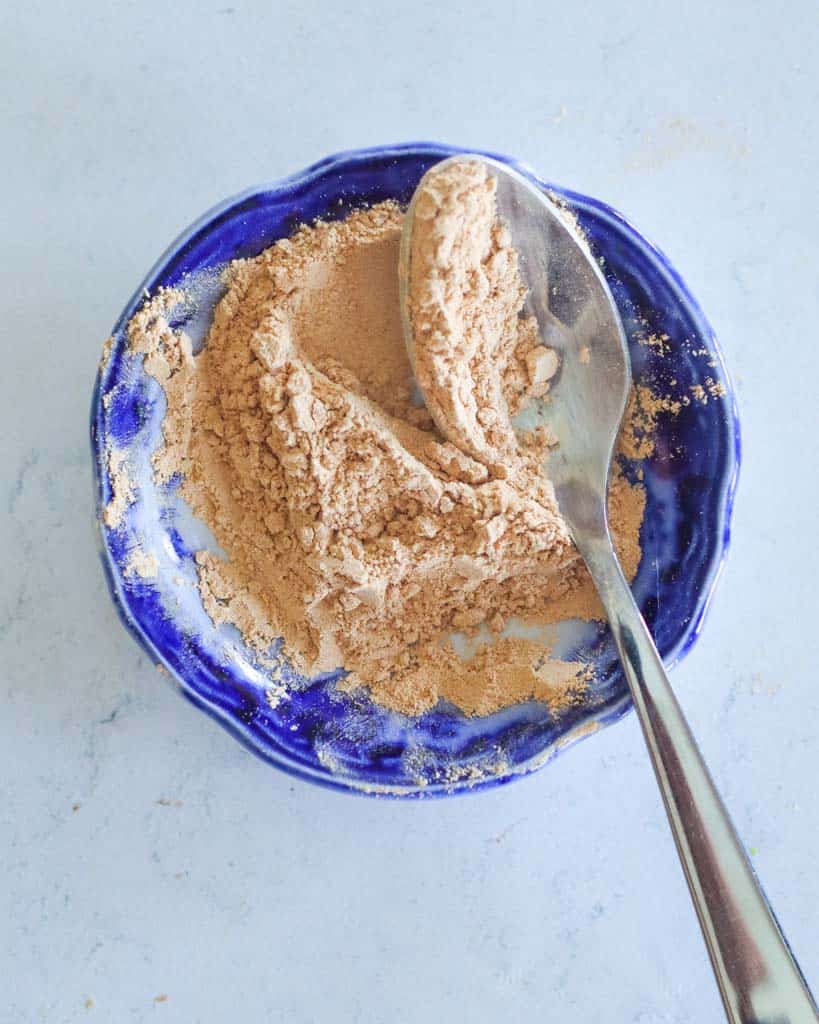 A small bowl of maca powder with a spoon in the bowl