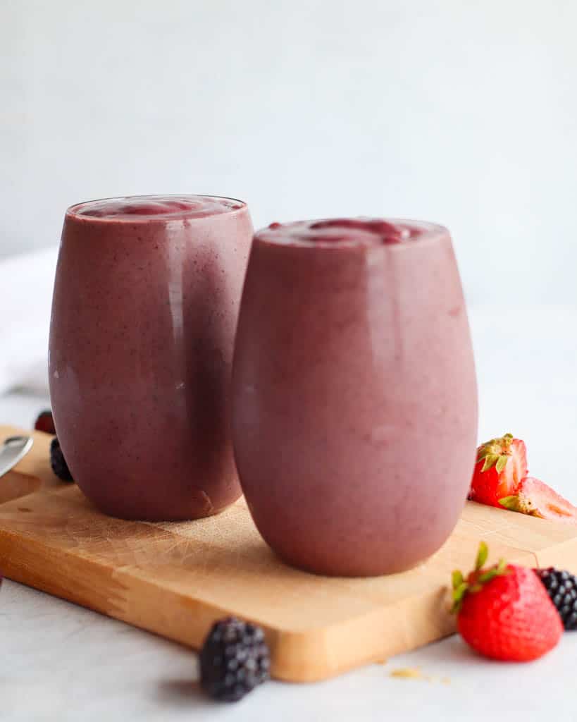 two glasses full of antioxidant smoothies with berries scattered around the cup