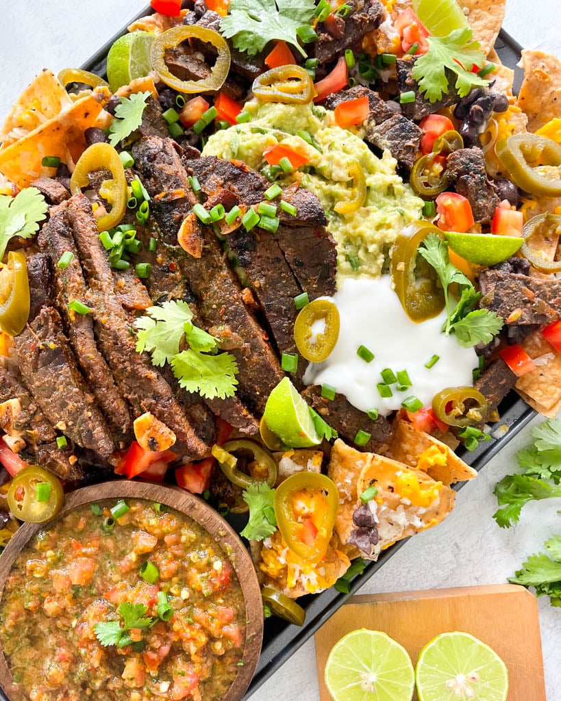 loaded carne asada nachos with beans, cheese, cilantro, guacamole, sliced jalapenos, with salsa served on the side