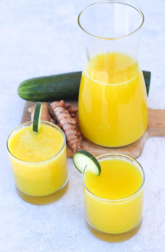 two glasses full of pineapple and cucumber juice garnished with slices of cucumber