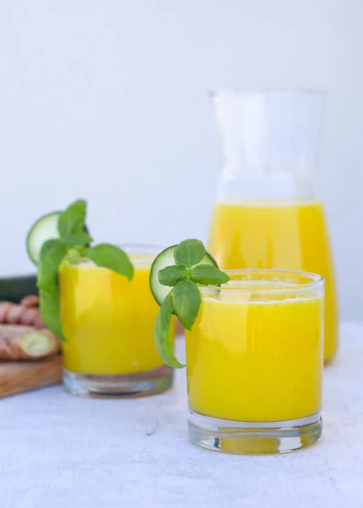 two glasses full of pineapple and cucumber juice garnished with a slice of cucumber and mint