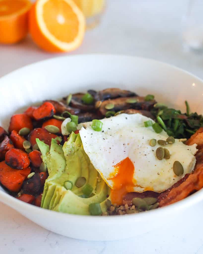 close up view of breakfast bowl with over easy egg, sliced avocado, and quinoa