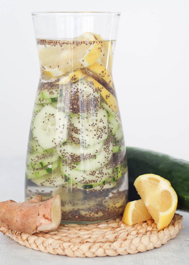 a carafe full of cucumber lemon ginger water with cucumber, ginger and sliced lemon beside it