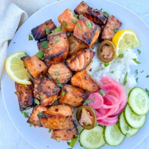 air fryer salmon bites on a plate with sliced cucumber rice and pickled onions