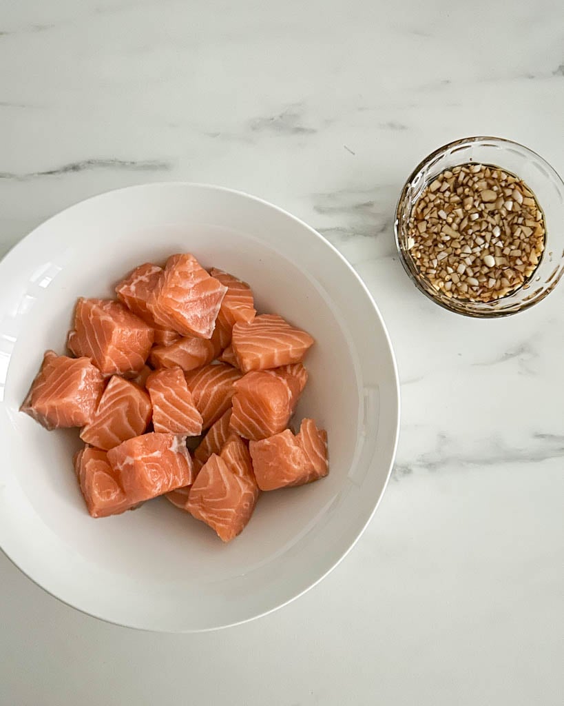 raw salmon pieces in a bowl with a small ramekin of marinade on the side