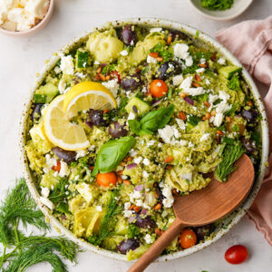large bowl of greek quinoa salad with large wooden spoon in the bowl