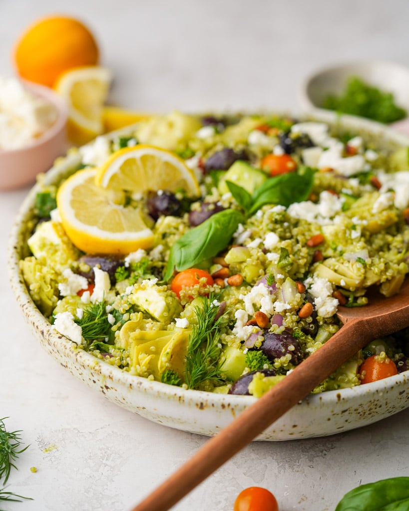 large bowl of greek quinoa salad with large wooden spoon in the bowl