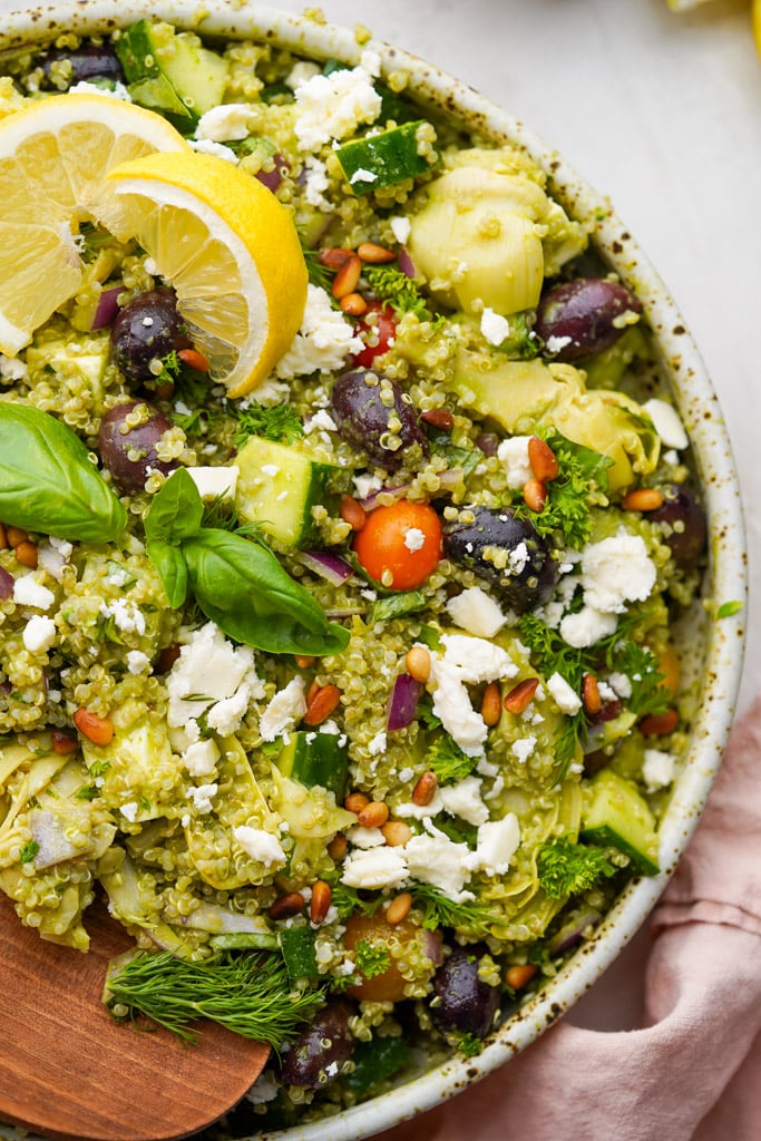 large bowl of greek quinoa salad with large wooden spoon in the bowl
