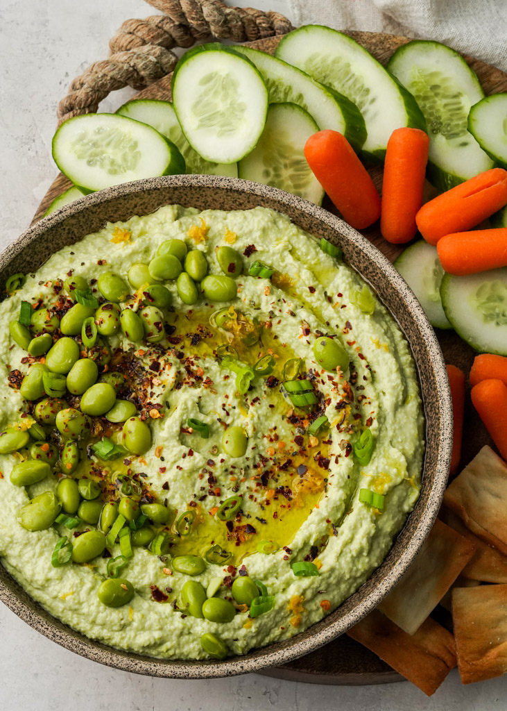 bowl of edamame hummus with assorted veggies and crackers on the side