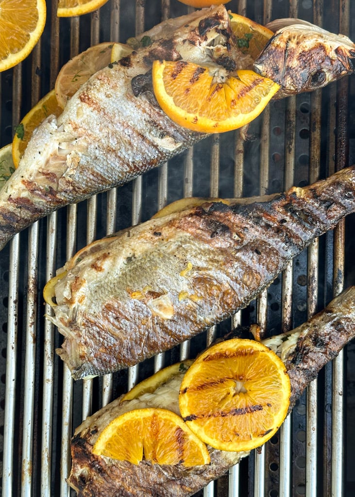 three pieces of whole stuffed branzino on the grill with lemon and orange slices