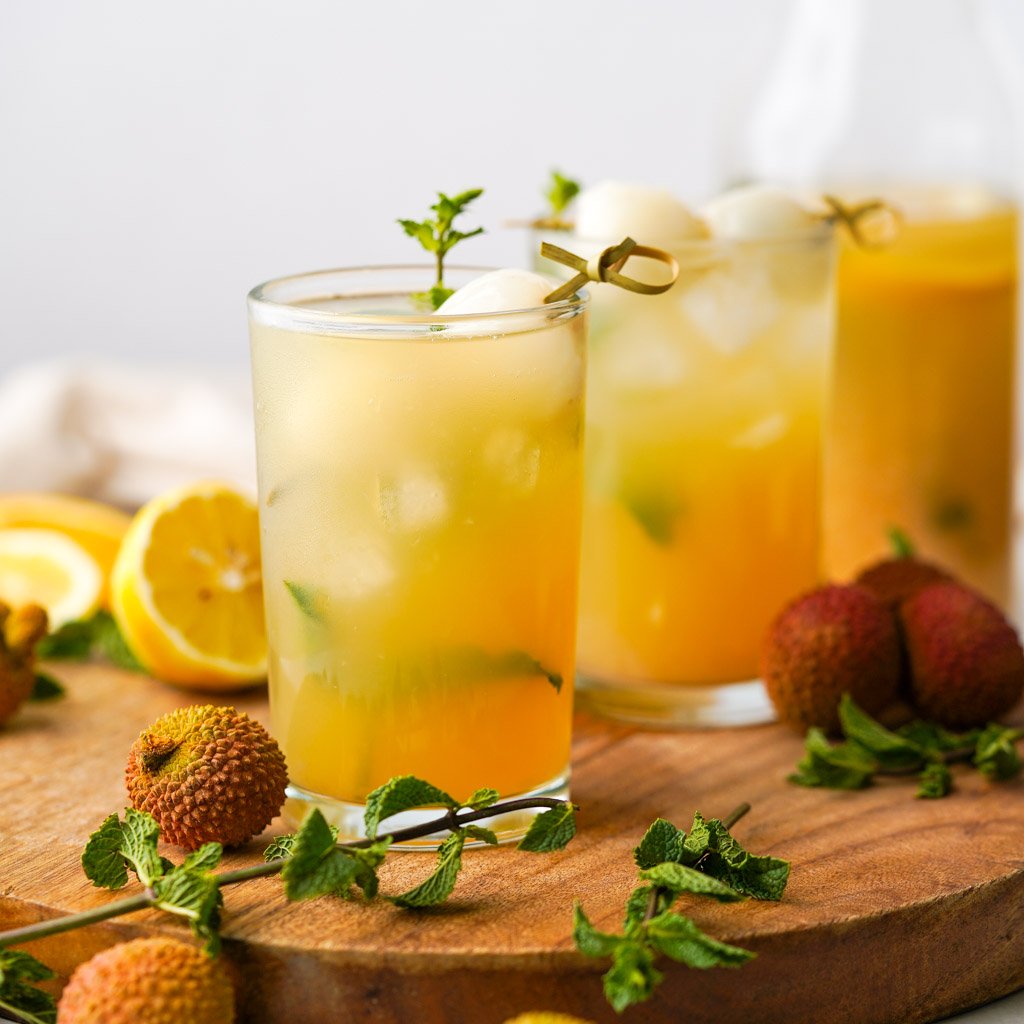 two glasses of lychee iced tea with lychee fruit and lemons scattered around