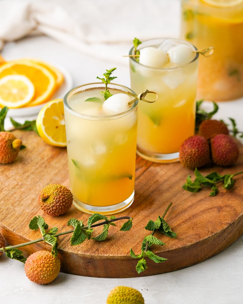 two glasses of lychee iced tea with lychee fruit and lemons scattered around