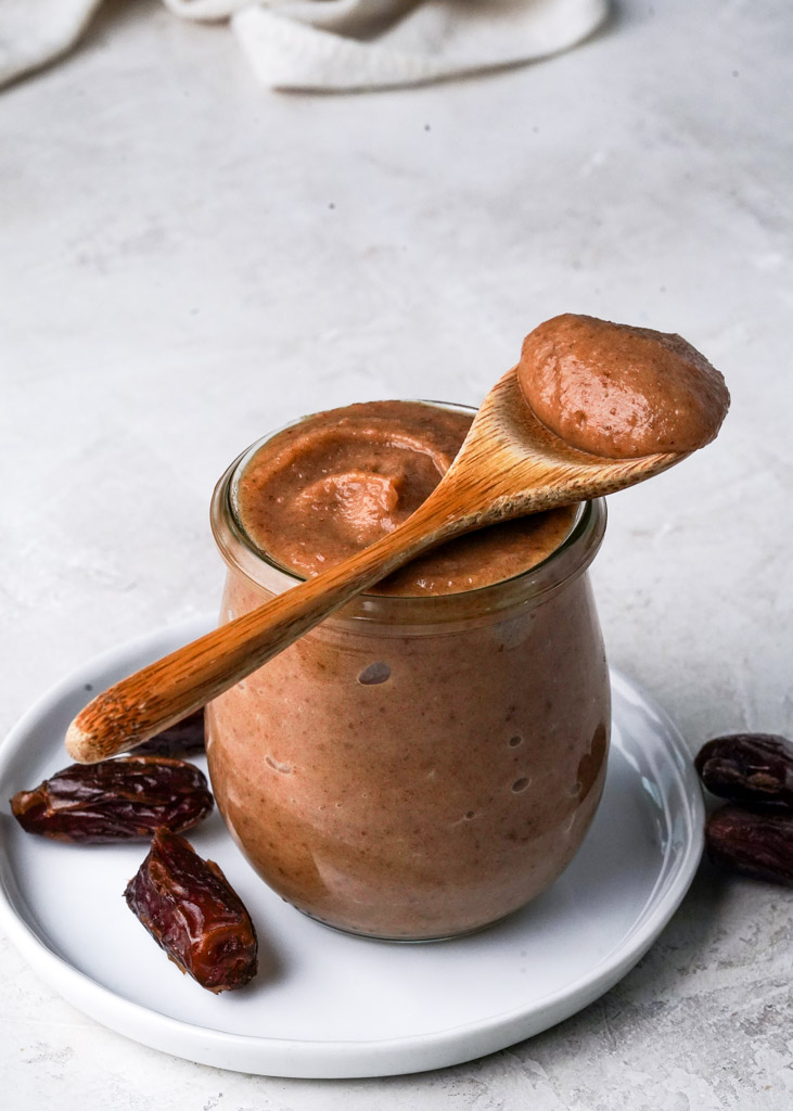 a spoonful of date caramel placed over a jar containing more, with dates on either side