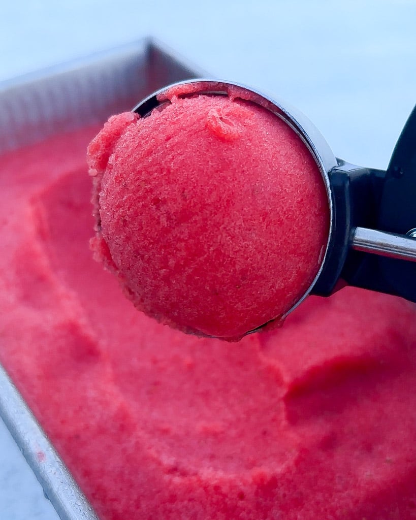 an ice cream scoop holding strawberry sorbet over a container with more