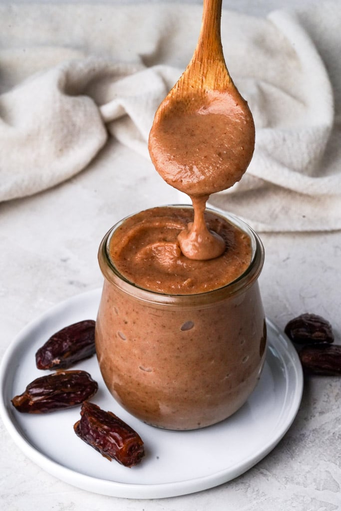 a spoonful of date caramel dripping down to jar containing more, with dates on either side