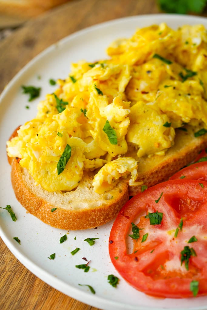 close up view of scrambled duck eggs on toast with a side of sliced tomatoes