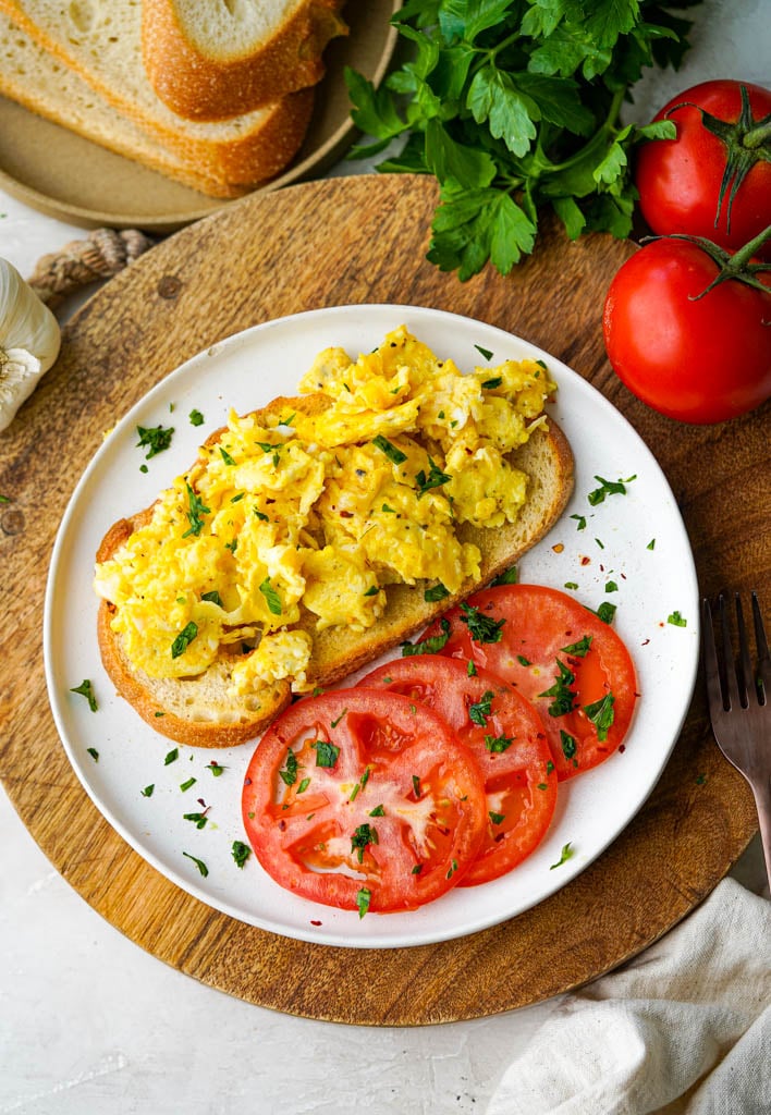 scrambled duck eggs on toast with sliced tomatoes on a white plate